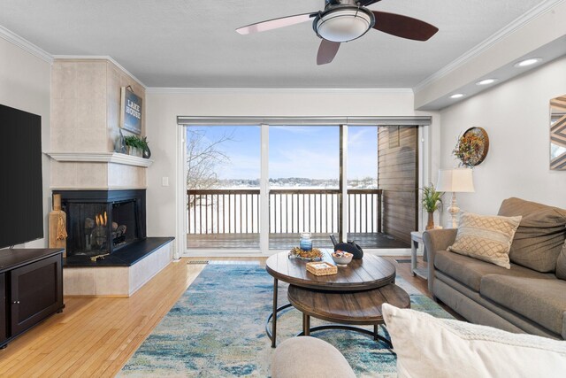 living room with ceiling fan, a tile fireplace, light wood-style flooring, and crown molding