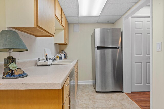 kitchen with backsplash, stainless steel appliances, light countertops, a paneled ceiling, and a sink