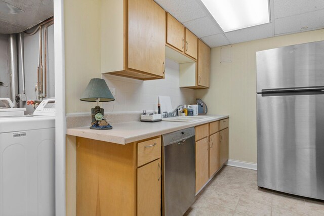 kitchen featuring independent washer and dryer, stainless steel appliances, light countertops, a paneled ceiling, and a sink