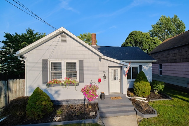 bungalow-style home featuring a chimney, fence, and roof with shingles