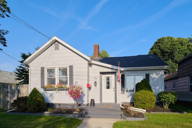 bungalow-style home featuring a chimney, a front yard, and fence