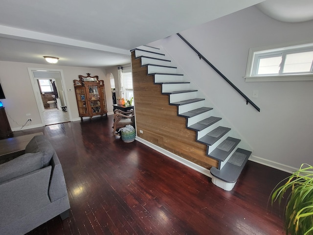 staircase featuring arched walkways, baseboards, and wood finished floors