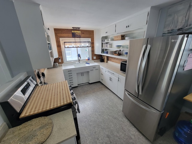 kitchen with decorative light fixtures, light countertops, freestanding refrigerator, white cabinetry, and wooden walls