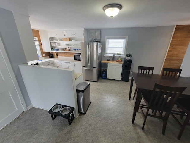 kitchen with black microwave, white cabinetry, light countertops, freestanding refrigerator, and light floors