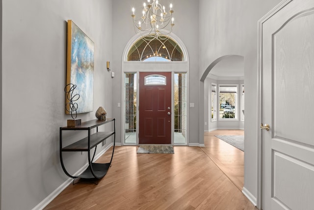 foyer entrance with baseboards, arched walkways, wood finished floors, and a towering ceiling