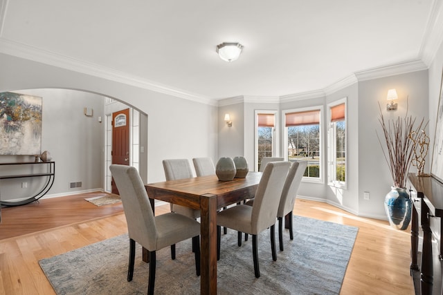 dining room with light wood-style flooring, visible vents, arched walkways, and baseboards