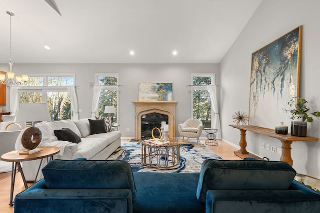 living area with a wealth of natural light, a glass covered fireplace, a chandelier, and wood finished floors