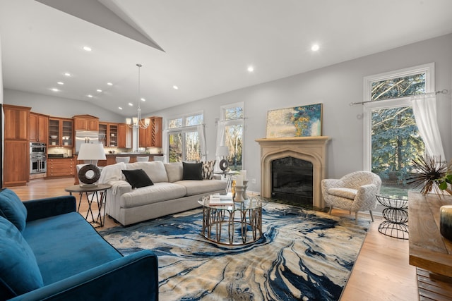 living room with a notable chandelier, a glass covered fireplace, recessed lighting, light wood-style floors, and vaulted ceiling