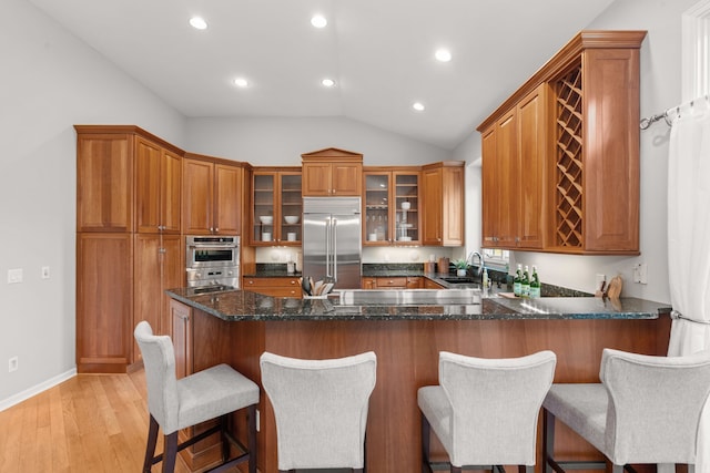 kitchen with brown cabinets, a sink, stainless steel appliances, a peninsula, and vaulted ceiling