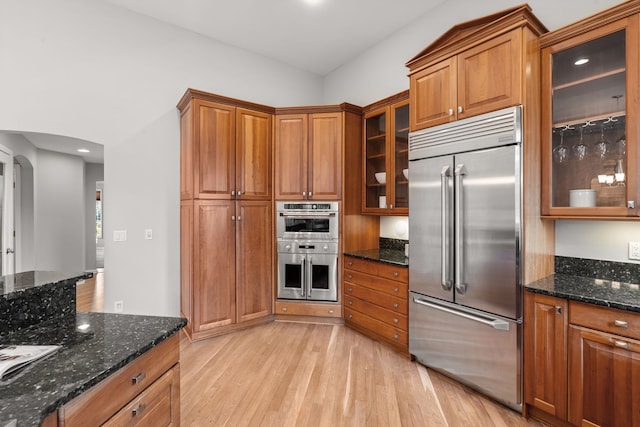 kitchen with brown cabinetry, light wood finished floors, appliances with stainless steel finishes, and arched walkways