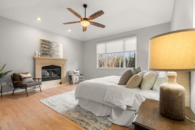 bedroom with light wood-type flooring, a ceiling fan, a glass covered fireplace, recessed lighting, and baseboards