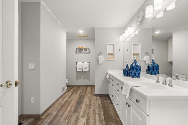 bathroom with a sink, wood finished floors, double vanity, and ornamental molding