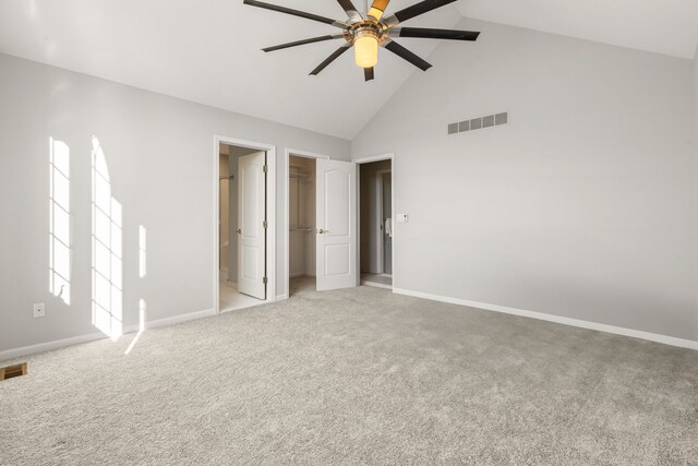 unfurnished bedroom featuring a walk in closet, baseboards, high vaulted ceiling, and visible vents