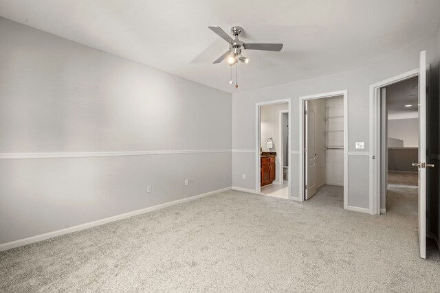 unfurnished bedroom with a walk in closet, baseboards, light colored carpet, and ensuite bathroom