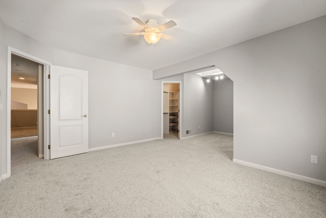 unfurnished bedroom featuring a walk in closet, a ceiling fan, a closet, carpet floors, and baseboards