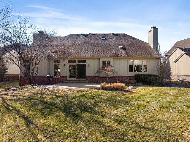 back of house featuring a shingled roof, a patio area, a lawn, and a chimney