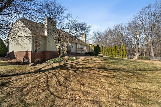 exterior space featuring fence, brick siding, a chimney, and a lawn