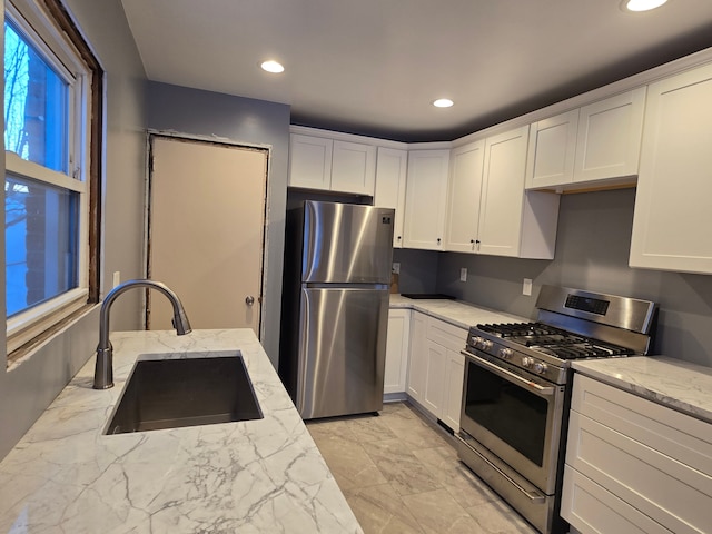 kitchen with a sink, light stone counters, appliances with stainless steel finishes, and white cabinets