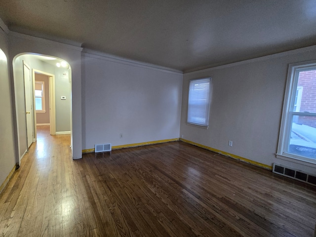 unfurnished room featuring arched walkways, dark wood-style floors, and visible vents