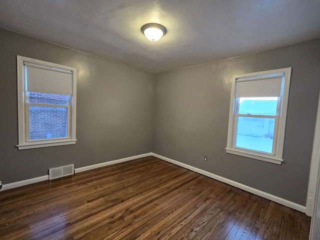 empty room featuring dark wood-style floors, baseboards, and visible vents