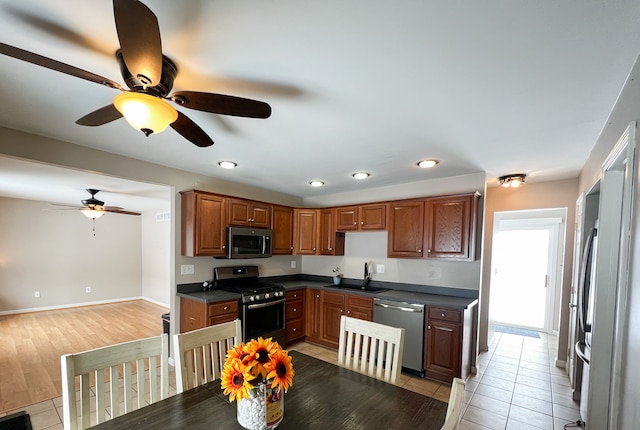 kitchen featuring light tile patterned floors, stainless steel appliances, a sink, brown cabinets, and dark countertops