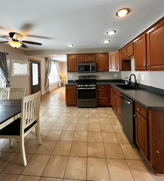 kitchen with appliances with stainless steel finishes, dark countertops, a sink, and light tile patterned floors