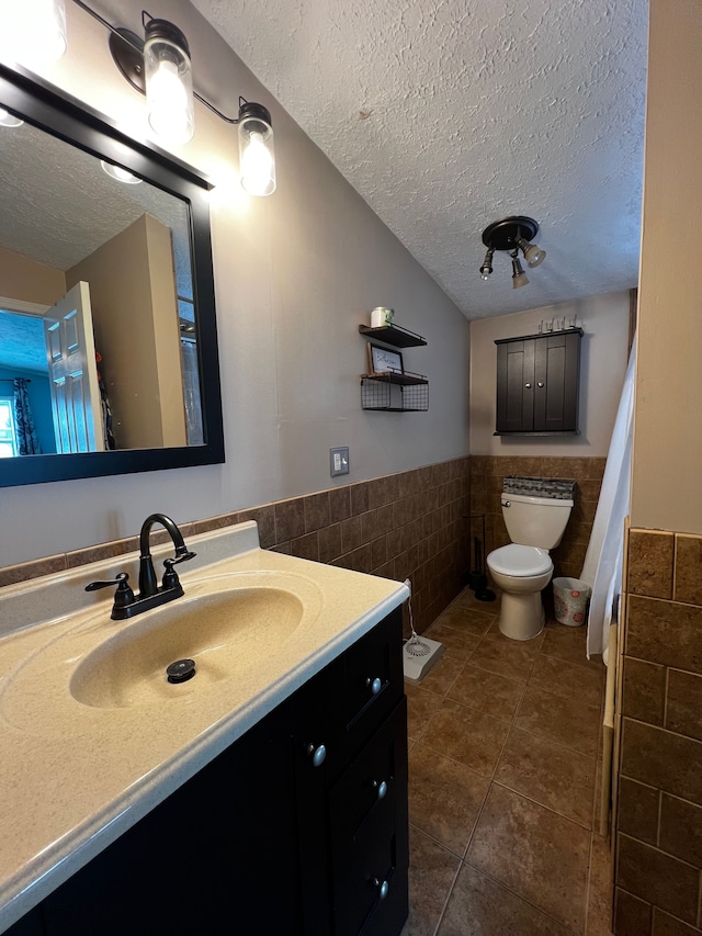 bathroom with toilet, a wainscoted wall, a textured ceiling, vanity, and tile walls