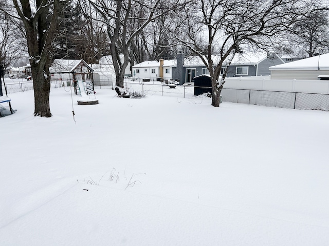 yard covered in snow with a residential view, fence, and a playground