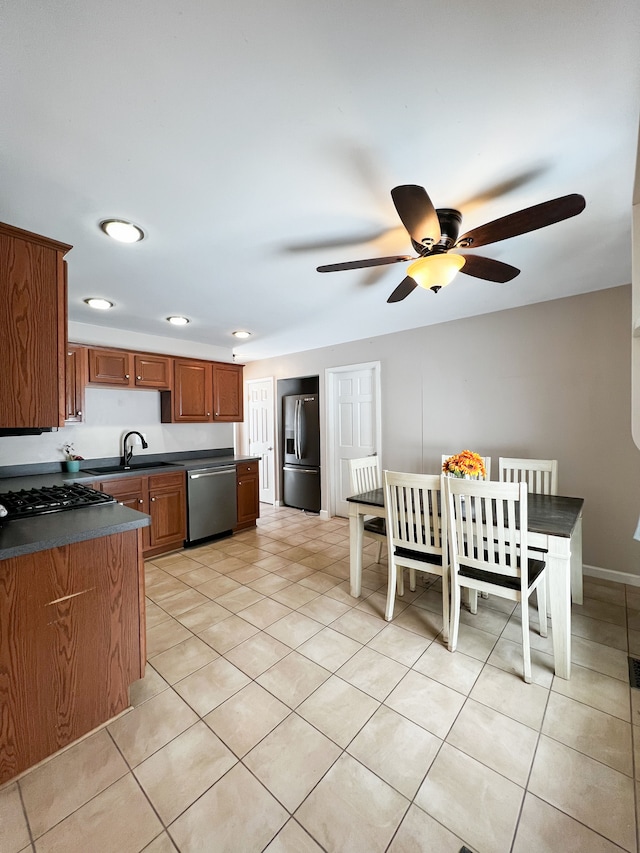 kitchen featuring light tile patterned flooring, stainless steel appliances, baseboards, brown cabinetry, and dark countertops