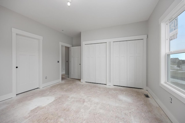 unfurnished bedroom featuring light colored carpet, two closets, visible vents, and baseboards