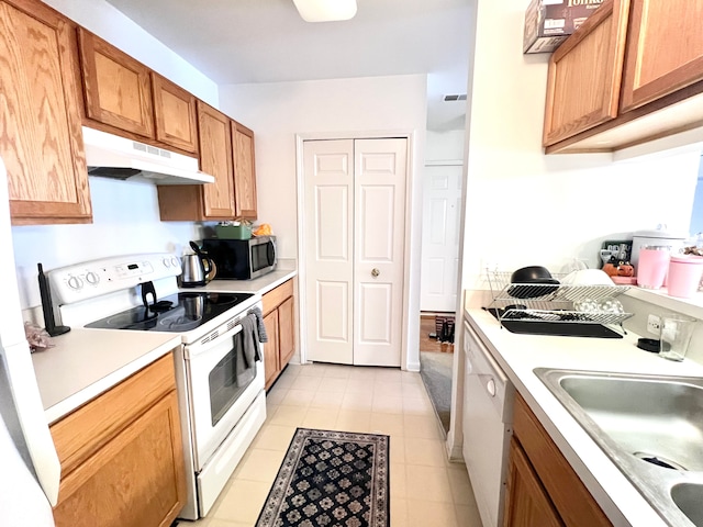 kitchen with white appliances, brown cabinetry, light countertops, under cabinet range hood, and a sink