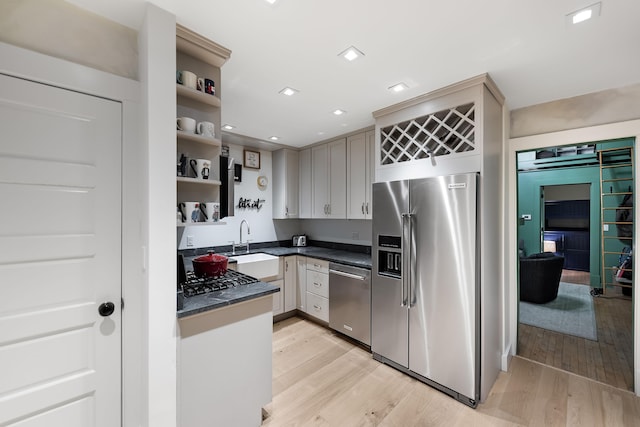 kitchen with dark countertops, stainless steel appliances, light wood-type flooring, and a sink