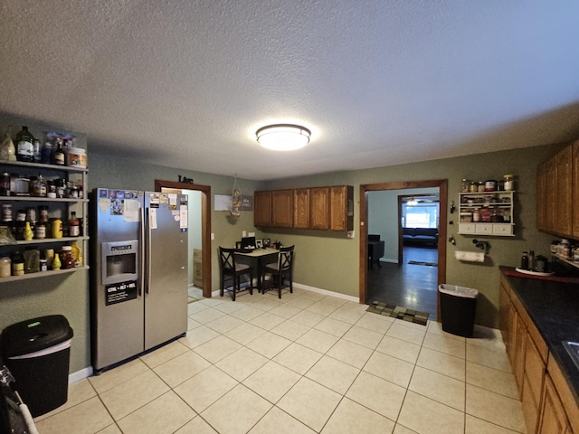 kitchen with brown cabinetry, dark countertops, stainless steel fridge, and light tile patterned flooring