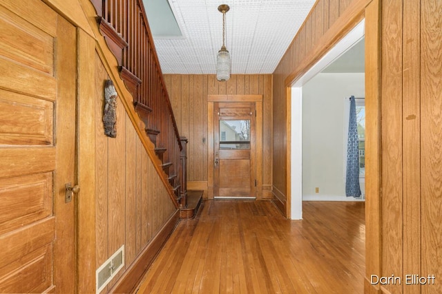 doorway with stairs, visible vents, wooden walls, and wood finished floors