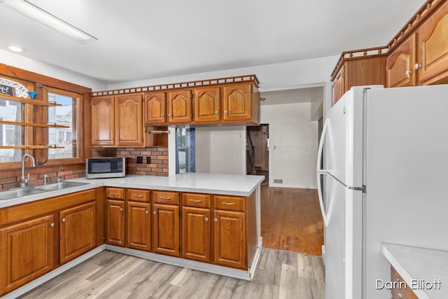 kitchen with light countertops, stainless steel microwave, freestanding refrigerator, a sink, and a peninsula