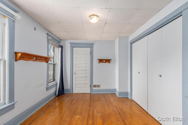 hall with baseboards, light wood-style flooring, visible vents, and a drop ceiling