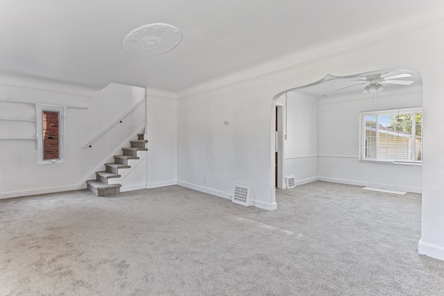 unfurnished living room with arched walkways, visible vents, a ceiling fan, stairs, and carpet