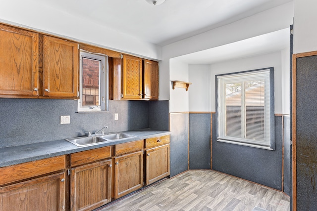 kitchen featuring light wood finished floors, dark countertops, a wainscoted wall, brown cabinets, and a sink