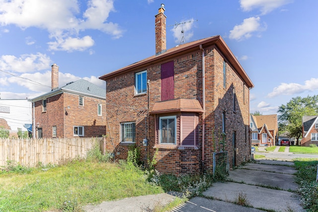 back of house with brick siding, fence, and a chimney