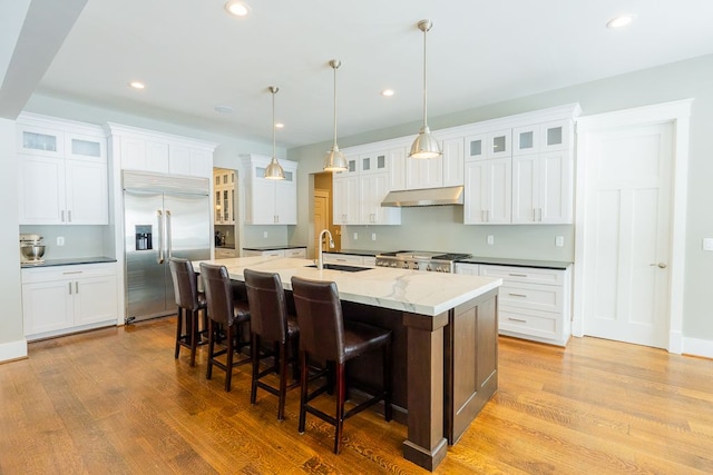 kitchen with built in refrigerator, white cabinetry, glass insert cabinets, and an island with sink