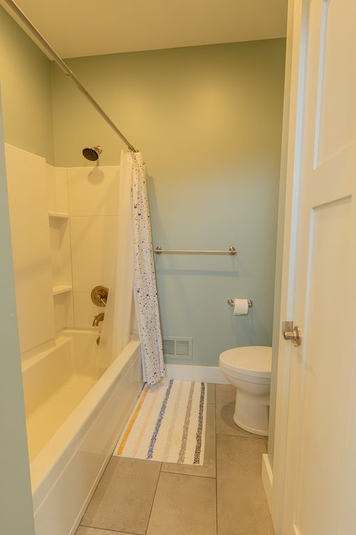 bathroom with visible vents, shower / bathtub combination with curtain, toilet, tile patterned flooring, and baseboards