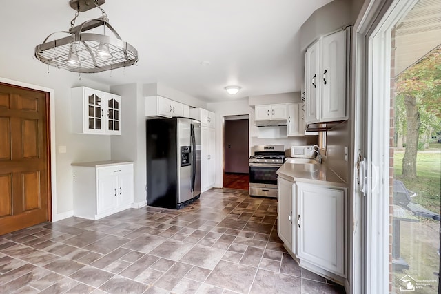 kitchen with under cabinet range hood, white cabinetry, light countertops, appliances with stainless steel finishes, and glass insert cabinets