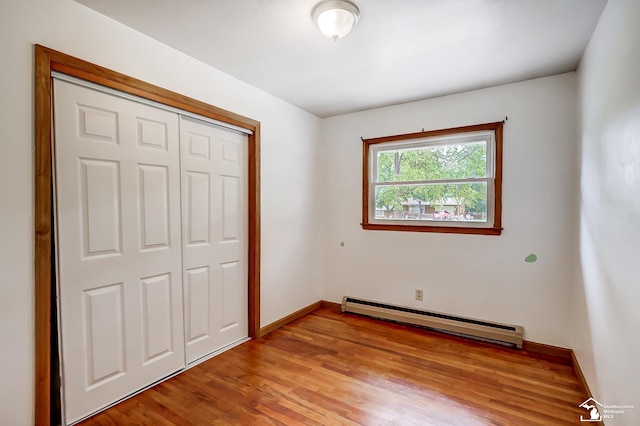 unfurnished bedroom featuring a baseboard heating unit, a closet, light wood-style floors, and baseboards