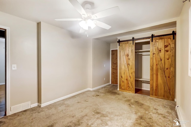 unfurnished bedroom with a baseboard radiator, visible vents, a barn door, carpet flooring, and baseboards