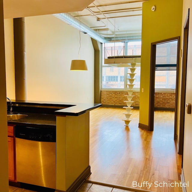 kitchen featuring dark countertops, brick wall, light wood-type flooring, stainless steel dishwasher, and a sink