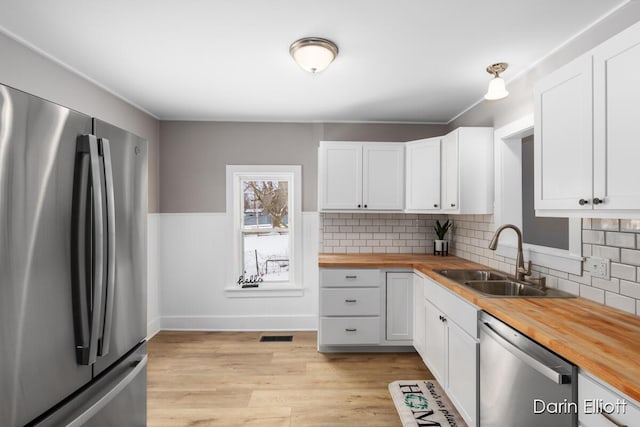 kitchen featuring stainless steel appliances, butcher block countertops, a sink, and white cabinets