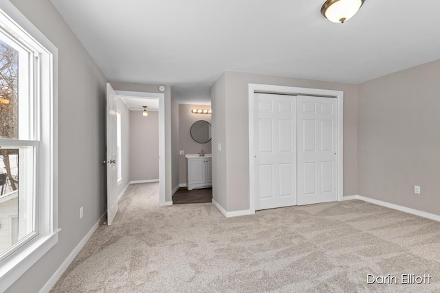 unfurnished bedroom featuring a closet, light colored carpet, ensuite bath, and baseboards