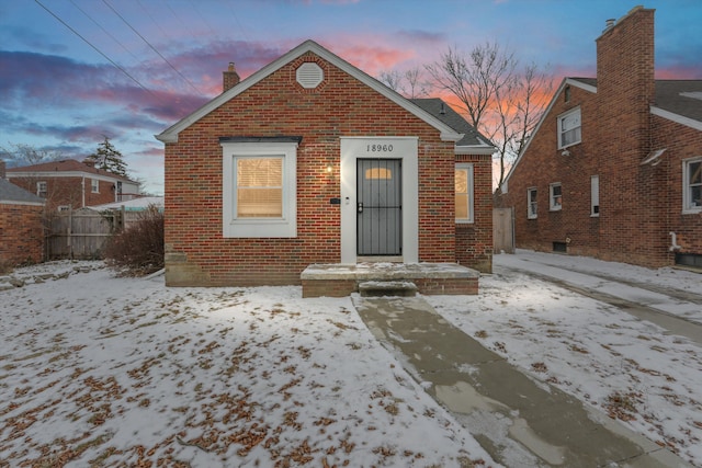 bungalow-style house featuring brick siding, a chimney, and fence