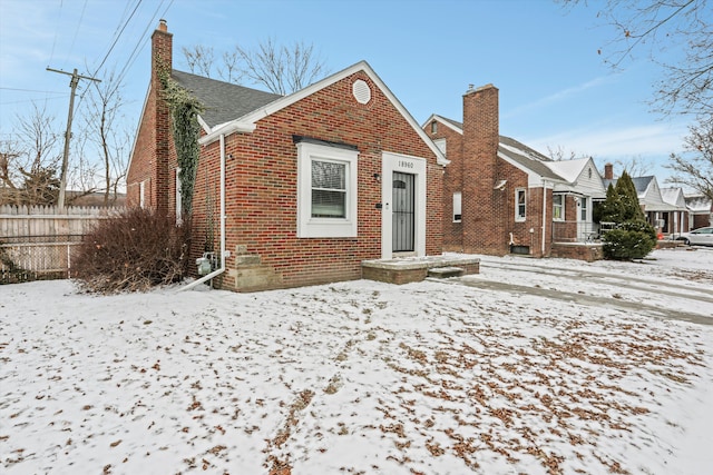 bungalow-style home featuring brick siding, fence, and a chimney