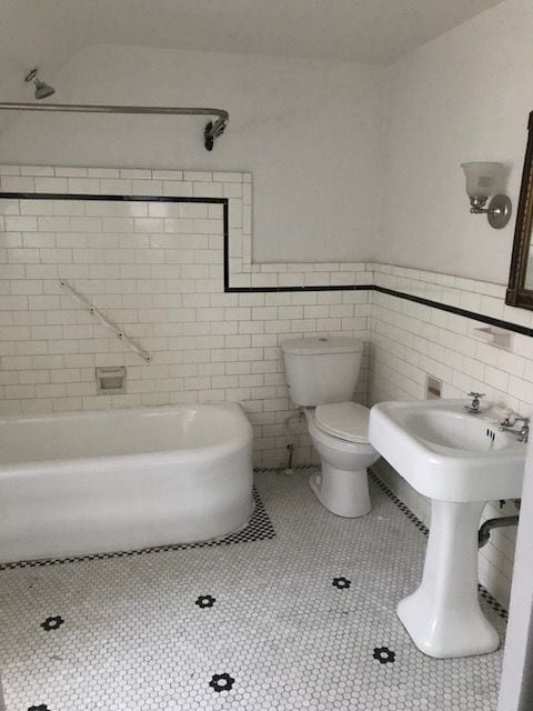 bathroom with a bath, tile walls, toilet, and tile patterned floors